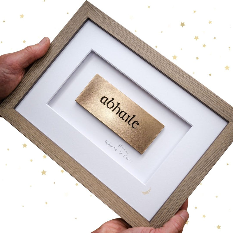 Framed gold nameplate with 'abhaile' inside, held by a hand on a white background.